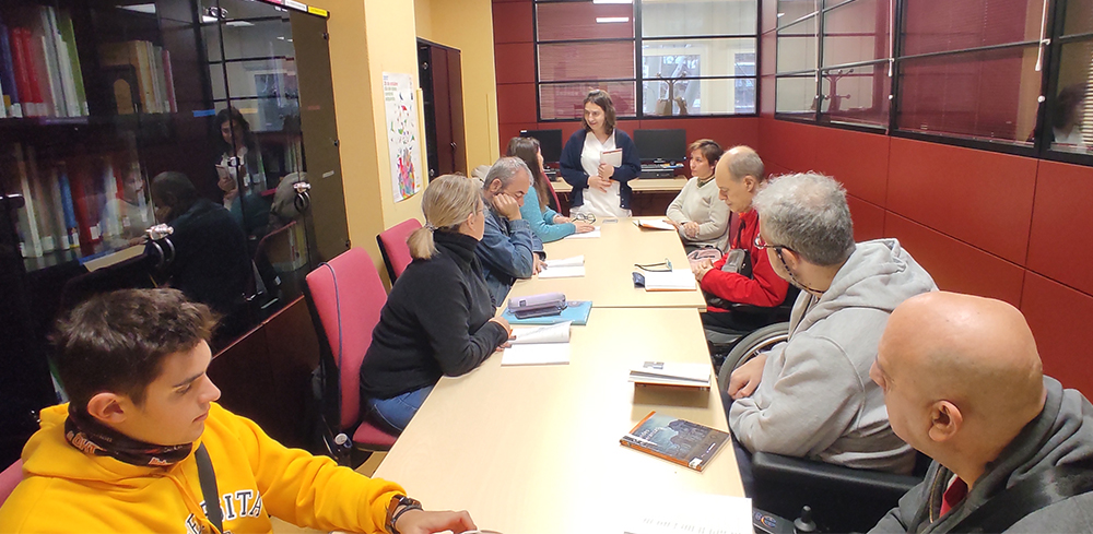 Personas usuarias del Ceadac en la biblioteca del centro durante el taller Club de Lectura Fácil. Con ellas está Silvia Martínez, TCAE del Ceadac.